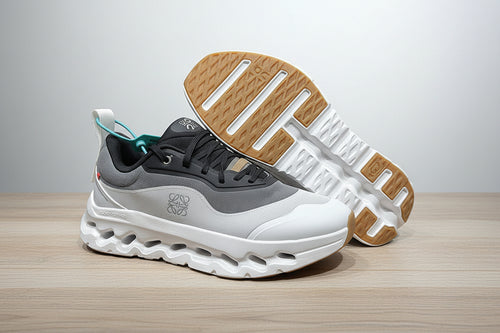 Gray and white sneakers with a brown sole on a light gray surface.